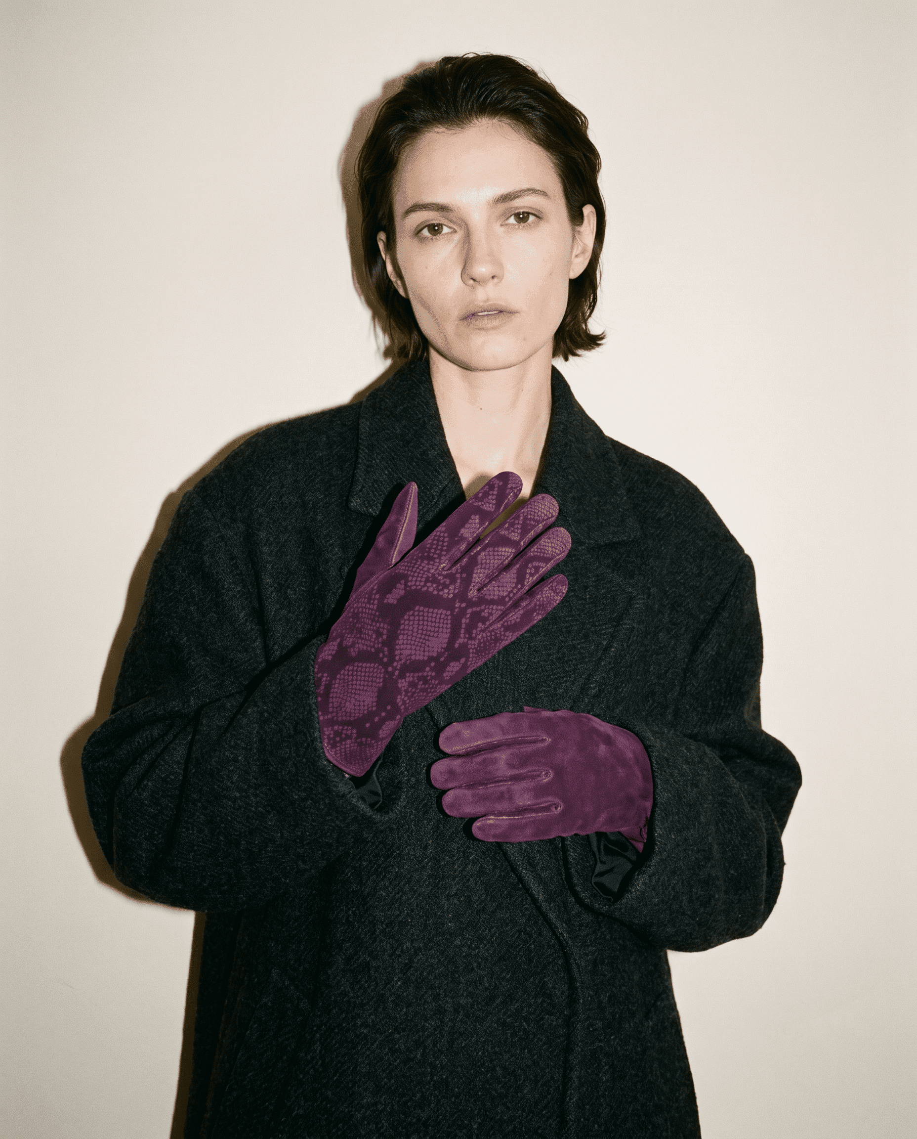 plum suede gloves with a python print, one hand at the collar of a charcoal wool coat