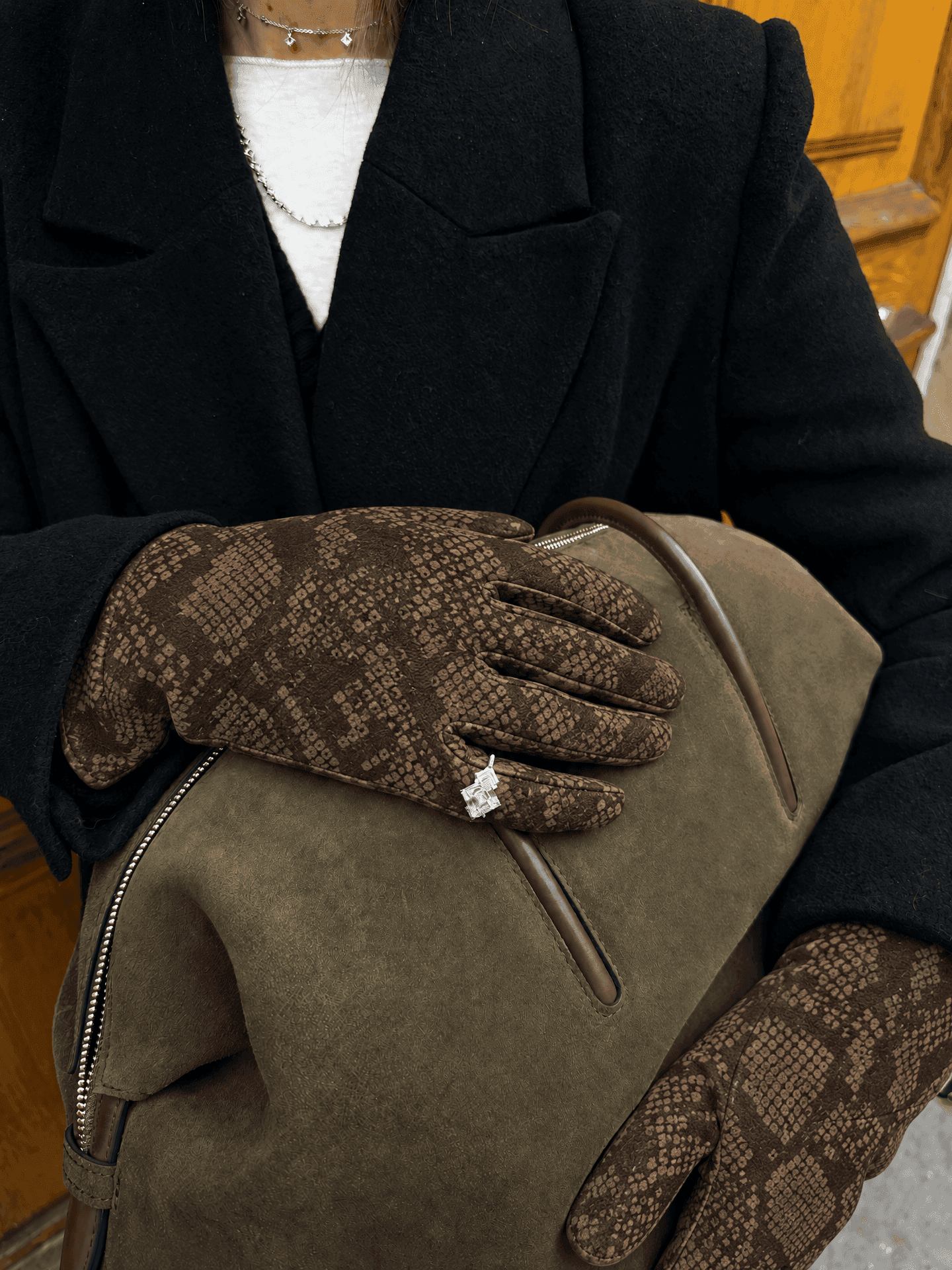 brown suede gloves printed with a python pattern, a silver ring worn over one glove, with a black coat and an olive suede bag