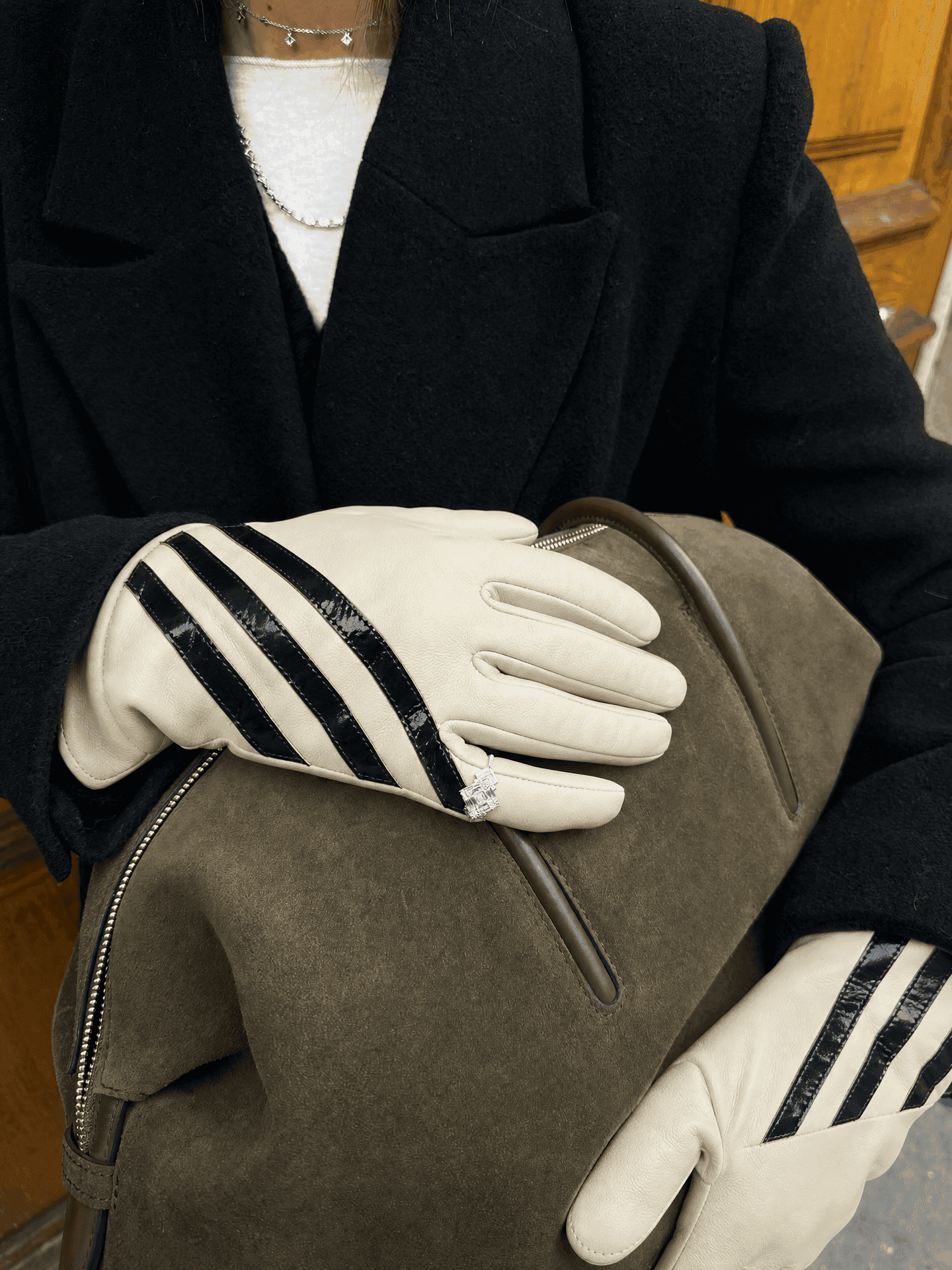 cream nappa leather gloves with three glossy black stripes worn with a black wool coat and an olive suede bag, a ring worn over one glove